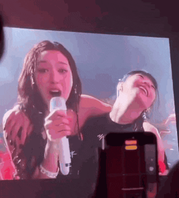 a couple of women are standing next to each other on a stage holding microphones and laughing .