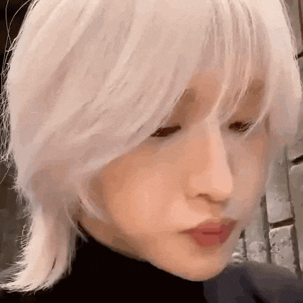 a close up of a person 's face with short white hair and a black turtleneck .