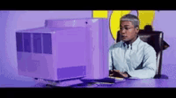 a man sits at a desk in front of a computer monitor with the letter u on the wall behind him