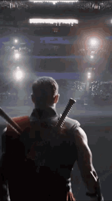 a man with a sword on his back is standing in a stadium looking at a crowd .