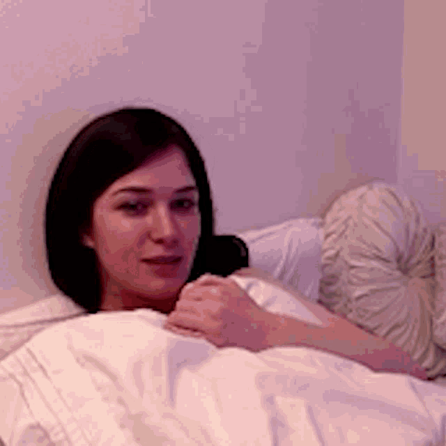 a woman laying in bed with a white comforter
