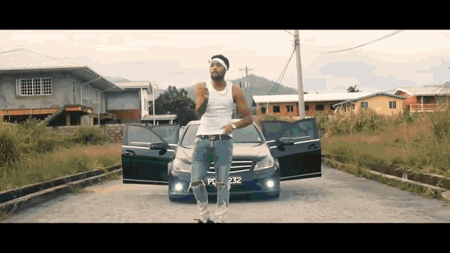 a man in a white tank top is standing in front of a black car with the license plate fc232