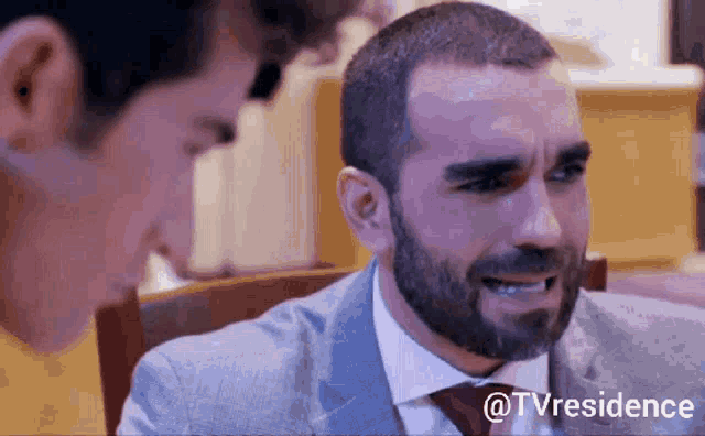 a man with a beard is crying while another man looks on .