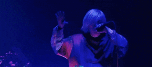 a woman with purple hair is singing into a microphone on a stage in front of a crowd .