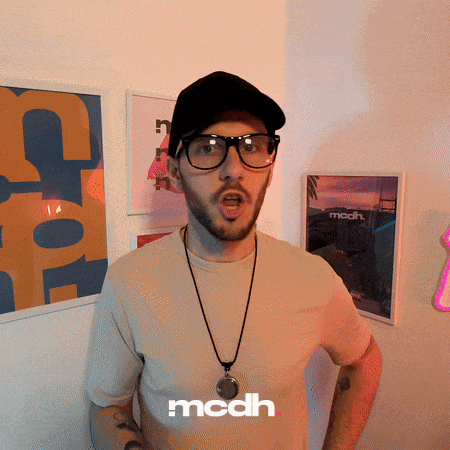a man wearing glasses and a hat is standing in front of a wall with a mcdh logo on it
