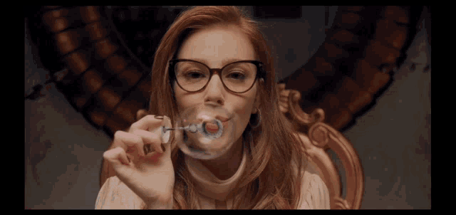 a woman wearing glasses blowing a soap bubble with the letter h on it