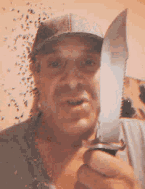 a man wearing a hat is holding a large knife in his hand .