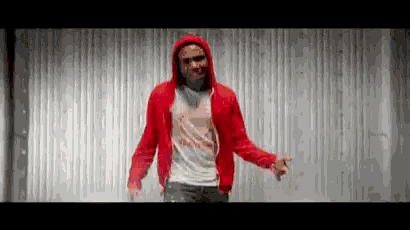 a man wearing a red hoodie is dancing in front of a wall .