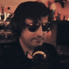 a man wearing sunglasses and headphones is standing in front of a microphone .