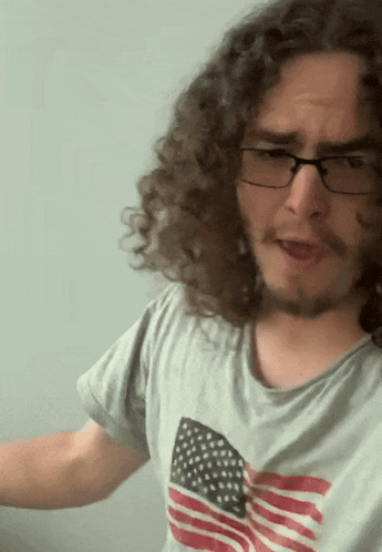 a man with curly hair wearing glasses and an american flag t-shirt