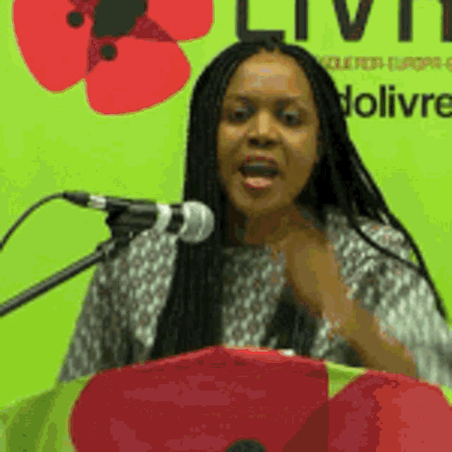 a woman stands at a podium with a microphone in front of a sign that says livi