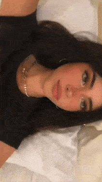 a woman wearing a black shirt and a pearl necklace is laying down on a bed