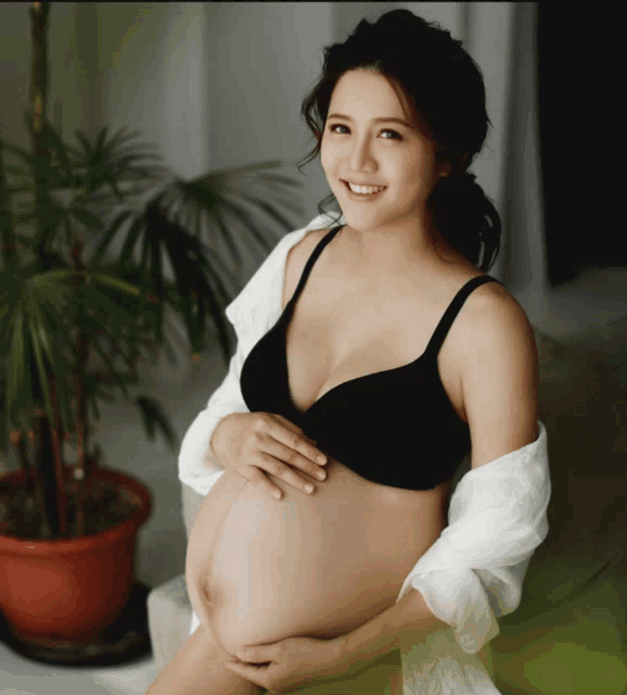 a pregnant woman in a black bra is sitting on a chair