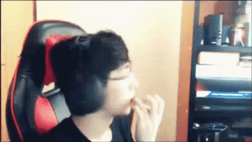 a man wearing headphones is sitting in a red and black chair eating a snack .