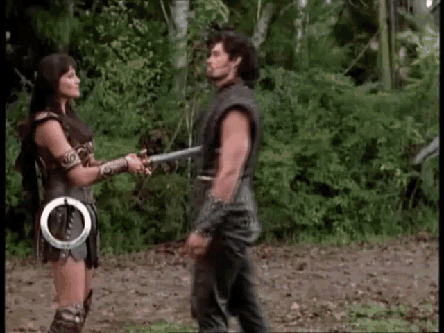 a man and a woman are standing next to each other in a forest holding swords .