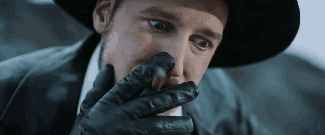 a man wearing a hat and gloves holds his nose