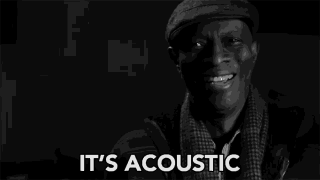 a man wearing a hat and scarf is smiling in a black and white photo and says `` it 's acoustic '' .