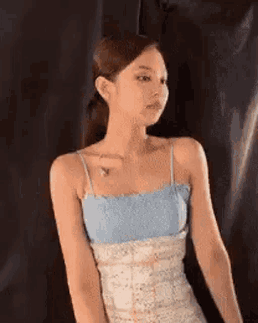 a woman in a blue tank top and white dress is standing in front of a black background .