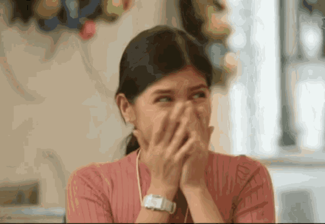 a woman wearing a pink sweater and a white watch is covering her mouth with her hands