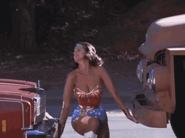 a woman in a wonder woman costume is kneeling down next to a red car