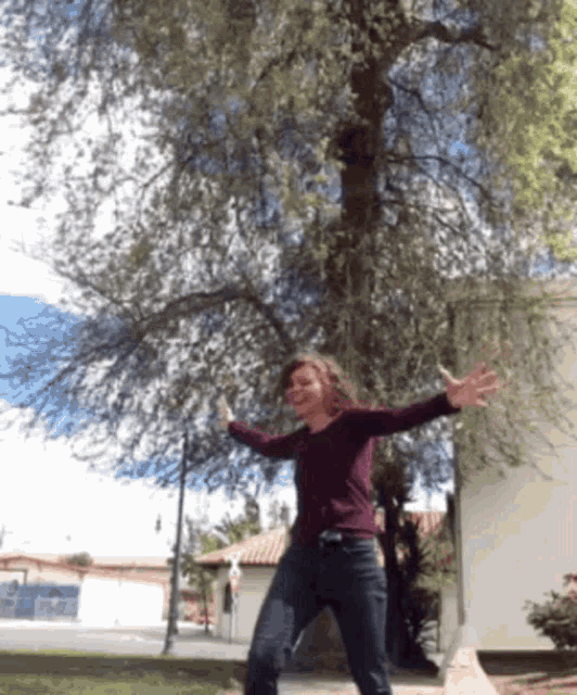 a woman with her arms outstretched stands in front of a tree