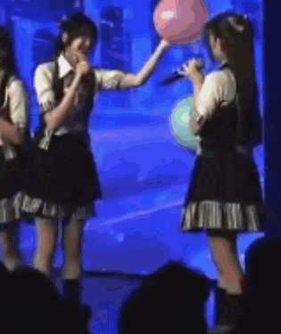 a group of girls are singing into microphones on a stage while holding balloons .