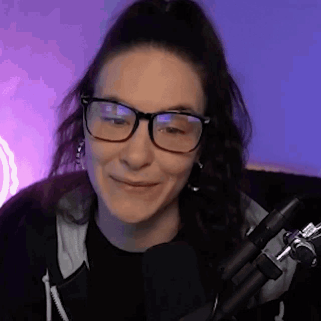 a woman wearing glasses and a black shirt is smiling in front of a microphone