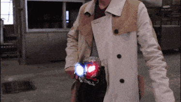 a man in a trench coat is holding a red and blue object in his hand