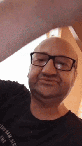 a bald man wearing glasses and a black shirt with the letters tmo on the sleeve