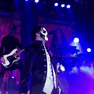 a man in a skull mask sings into a microphone while holding a guitar
