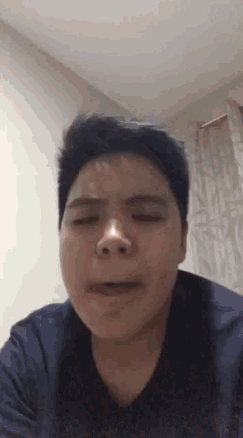 a young man in a blue shirt is making a funny face with his eyes closed .