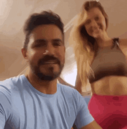 a man with a beard is taking a selfie with a woman in a sports bra