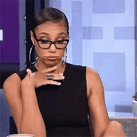 a woman wearing glasses and hoop earrings is sitting at a table making a funny face .