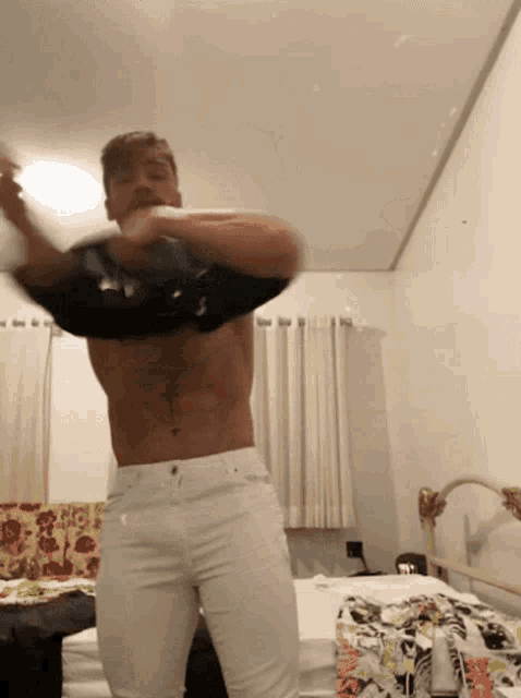 a shirtless man is standing on a bed with his shirt off