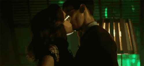 a man and woman are kissing in a dark room in front of a green light .