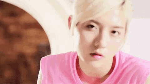 a young man with blonde hair is wearing a pink tank top and making a funny face .