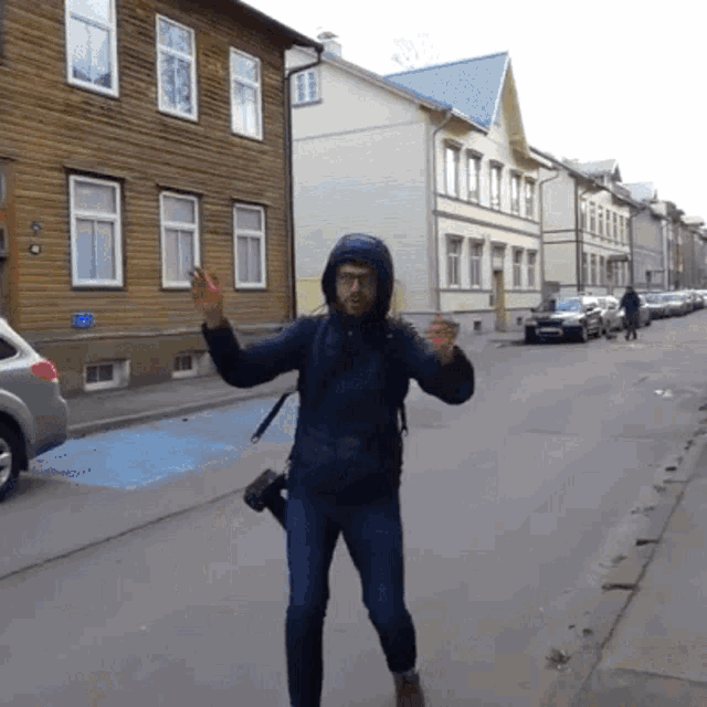 a man in a hooded jacket is walking down a street in front of a building with a blue sign on it