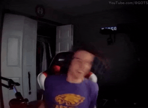 a man wearing a purple shirt with a yellow eagle on it is standing in a dark room .