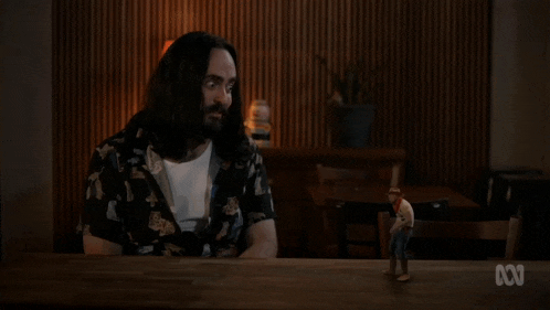 a man with long hair sits at a table with an abc logo on the bottom left