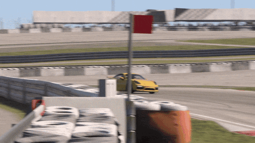 a yellow car is driving down a race track with a red flag in the foreground