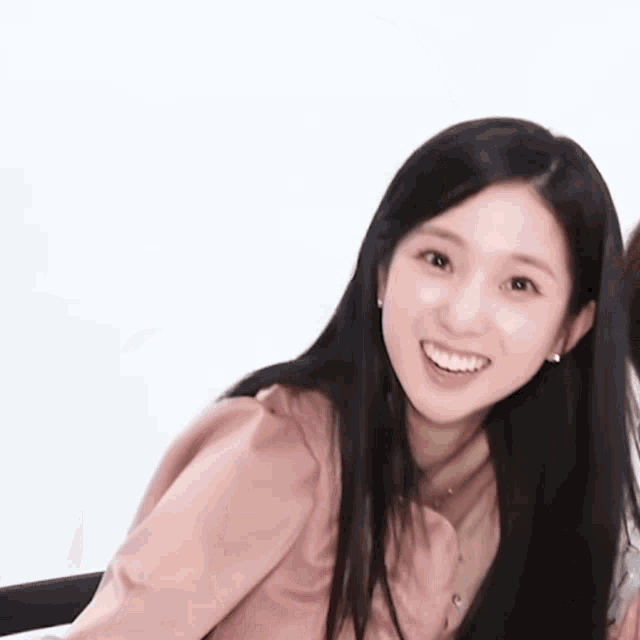 a woman with long black hair is smiling and wearing a pink shirt .