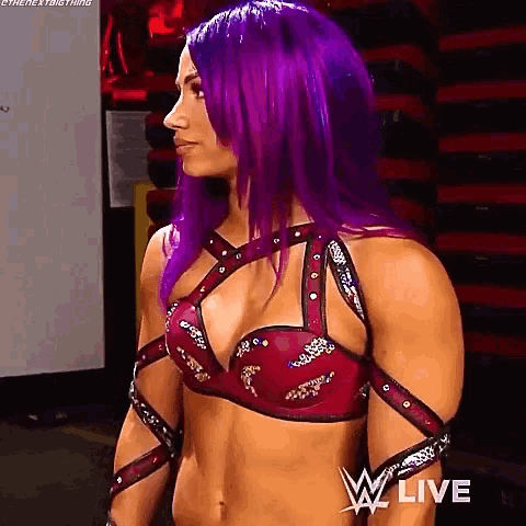 a woman with purple hair is wearing a red bra and standing in front of a wall .