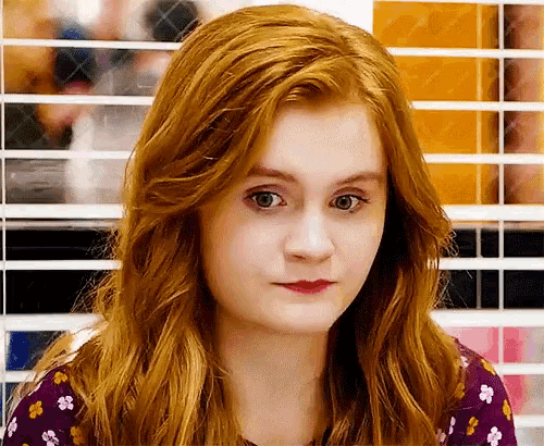 a young woman with red hair is making a funny face while wearing a floral shirt .