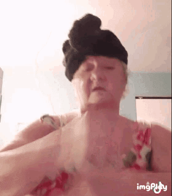 an older woman wearing a black hat and a floral top is making a funny face .