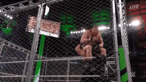 a wrestler is jumping over a fence in a cage during a wrestling match .