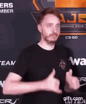 a man with a beard is giving a thumbs up in front of a cs go sign .