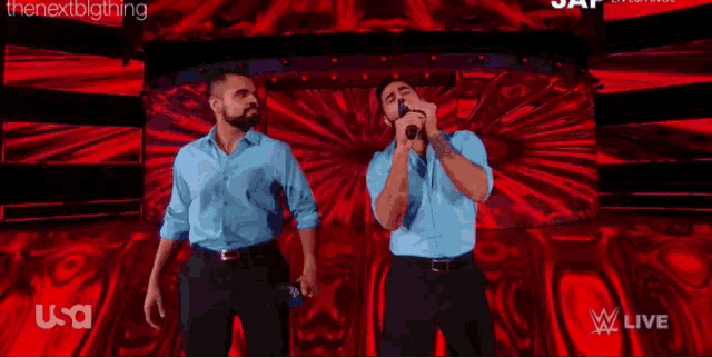 two men singing into microphones on a stage in front of a screen that says w live