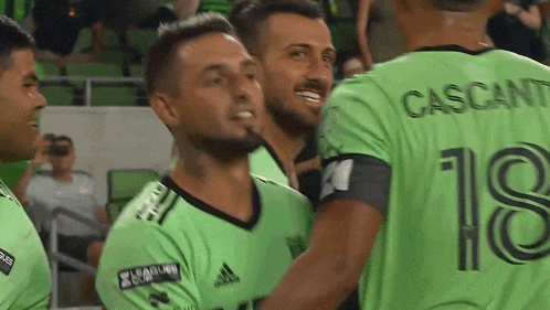 a group of soccer players wearing green jerseys with the number 18 on them are hugging each other .