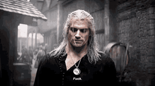 a man with long white hair is wearing a necklace and a black shirt and is standing in front of a brick building .