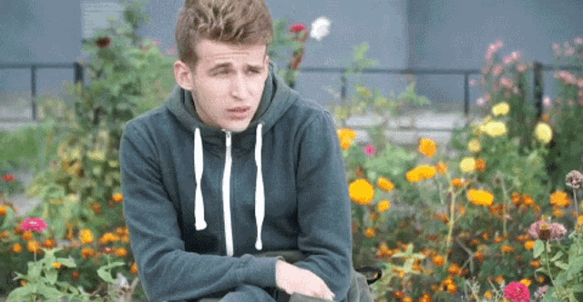 a young man in a green hoodie is sitting in front of a flower garden .